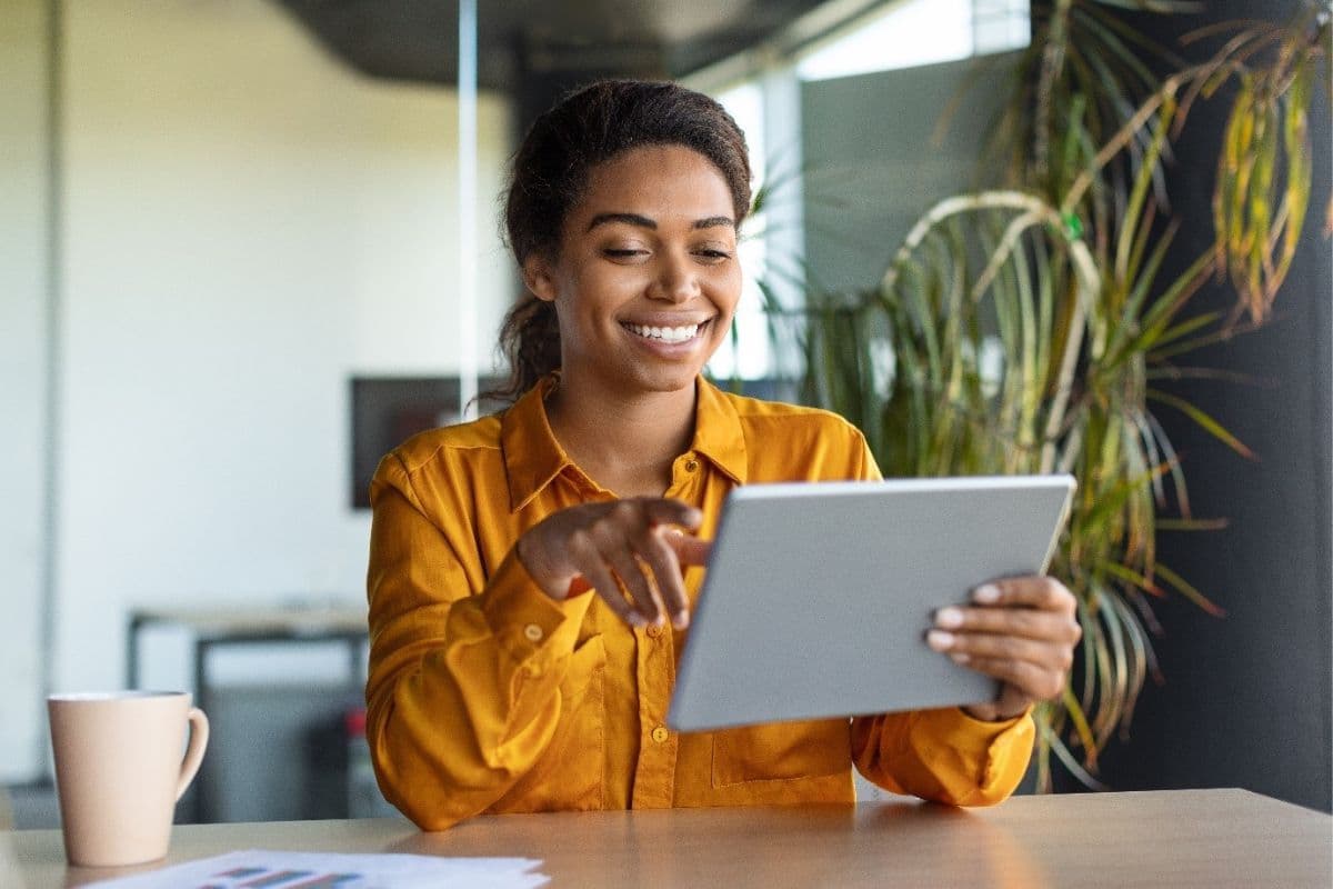 Woman in yellow smiling while holding tablet 