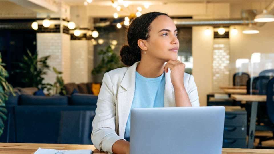 Woman in blue blouse and white blazer, sitting at desk with laptop