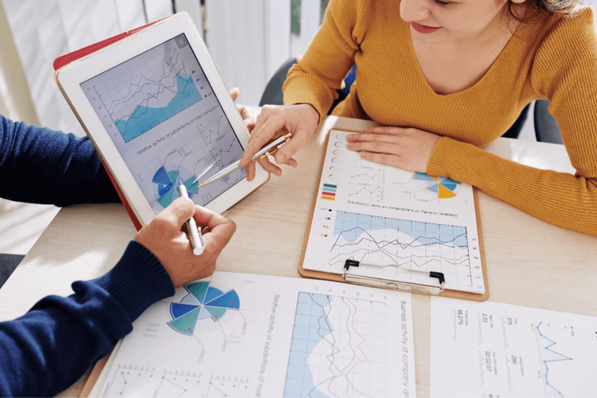 People sitting at desk looking at statistic sheets on clipboard and tablet.