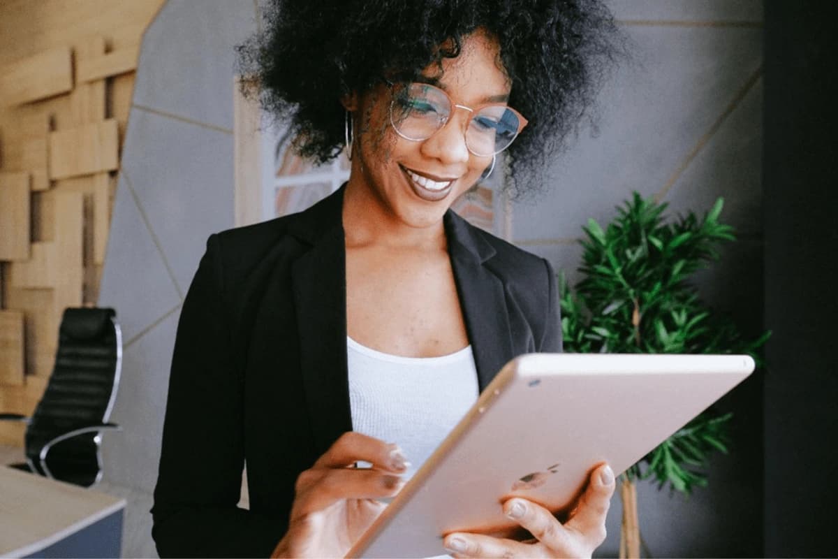 Woman with black blazer, wearing glasses while looking at tablet.