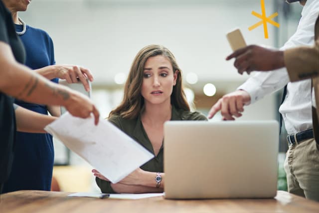 Woman at desk surround by people looking stressed 