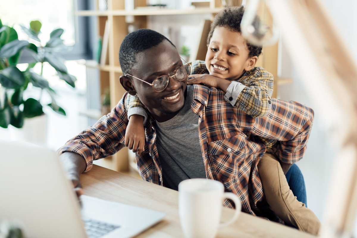 Dad working on laptop while child climbs on back
