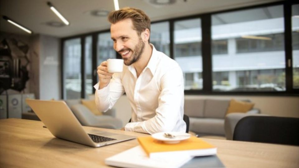 Man at desk with cup of coffee smiling at laptop